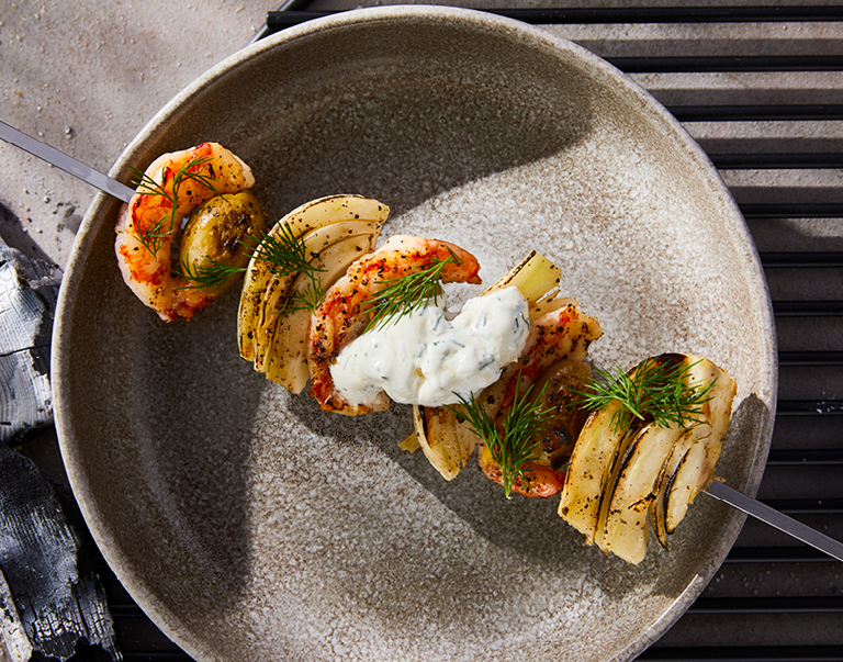 Gegrilde spies met Argentijnse garnalen, venkel en groene olijven. Geserveerd met Griekse yoghurt, dille en ingelegde citroen.