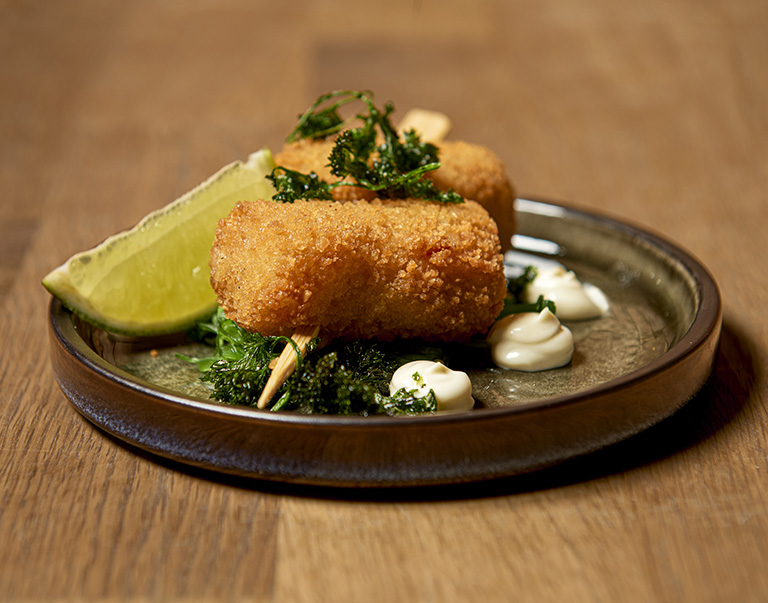 Mini-gambacroquet op een spiesje met wakame, limoenkoriandermayonaise en limoen. Perfecte snack met frisse smaken en een knapperige afwerking.