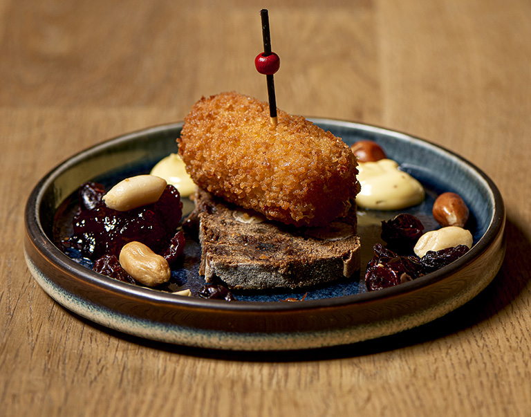 Mini-kaascroquet op kletsenbrood met cranberrycompote en mosterdmayonaise. Luxe borrelhap met zoet-pittige smaken en een feestelijke presentatie!