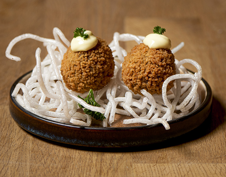 Plant-based bitterballen op een knapperig noedelnestje, gegarneerd met romige vegan mayo. Een heerlijke, vegan snack met een verrassende presentatie!